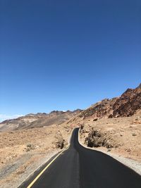 Road amidst mountains against clear blue sky