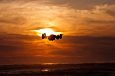 Silhouette drone flying against sky during sunset