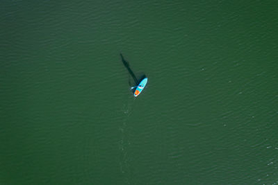 Drone view of sup board with traveler floating on calm water surface of green color on sunny day in spain