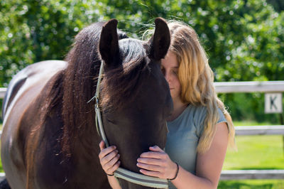 Close-up of teenage girl holding horse while standing on field