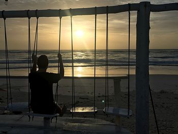 Rear view of man sitting at beach during sunset