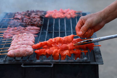 Cropped image of person preparing meat on barbecue grill