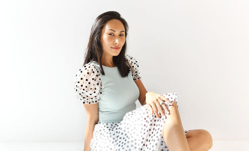 Young woman looking away while sitting against white background