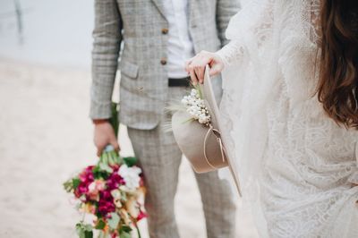 Midsection of bride with bridegroom holding hat