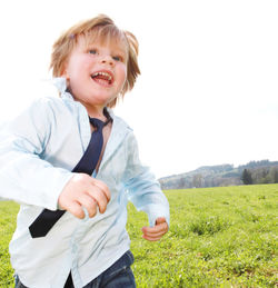 Happy boy running on grassy field against clear sky