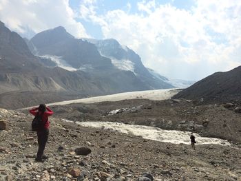 Female hiker standing on mountain against cloudy sky at athabasca glacier