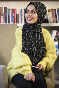 Smiling young woman wearing hijab sitting on chair at home