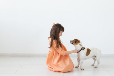 Girl with dog sitting on floor against wall