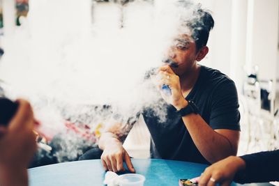 Young man smoking electronic cigarette while sitting at table