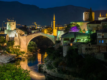 Arch bridge over river against buildings at night