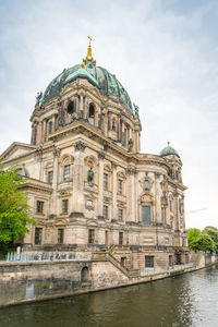 Facade of berlin cathedral by spree river against sky