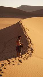 Side view of shirtless man with camera standing at desert during sunny day