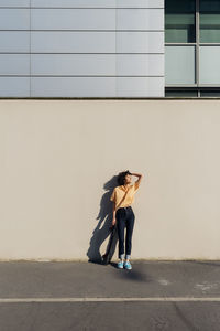 Woman with head in hand standing by wall on sunny day