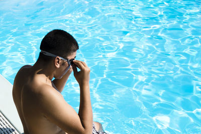 High angle view of shirtless man wearing goggles while sitting by pool
