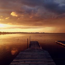 Jetty by sea against cloudy sky during sunset