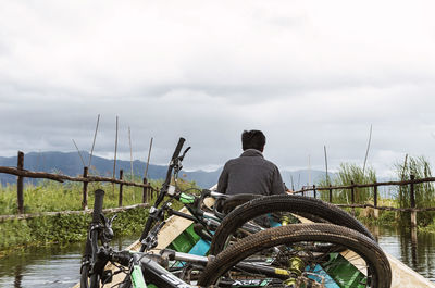 Nyaungshwe, myanmar - 04.17.2017: faceless male carrying bicycles on wooden boat floating through grassy fenced shores on inle lake on overcast day