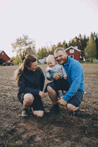 Parents with toddler son crouching at farm during sunset