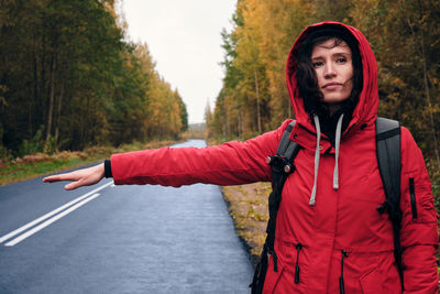 Portrait of young woman standing on road against trees