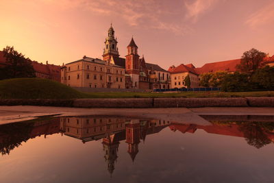 Lake by church against sky during sunset