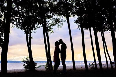 Silhouette couple kissing amidst trees at beach during sunset