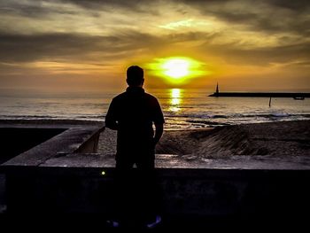 Rear view of silhouette man on beach against sky during sunset