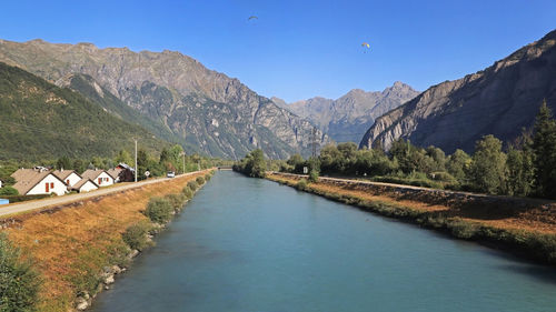 Scenic view of river by mountains against blue sky