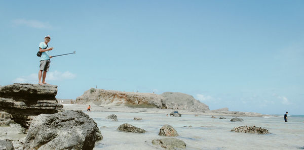 People standing on rock by sea against clear sky