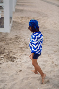 Boy child walks on the beach with sand on a chaise longue in a blue striped jacket and sunglasses