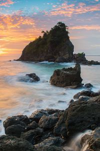 Rocks on beach against sky during sunset