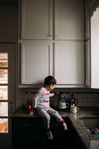 Young boy sitting on kitchen counter turning on coffee machine