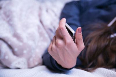 Cropped image of woman holding mobile phone on bed