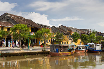 Boats moored on canal by buildings against sky