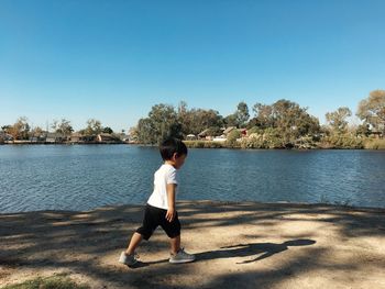 Full length of boy standing on lake against clear sky