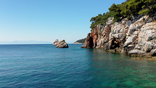 Scenic view of rocks in sea against clear blue sky