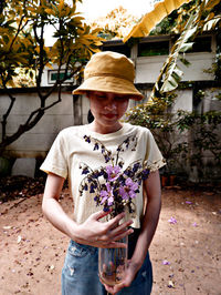 Portrait of woman holding hat while standing against plants