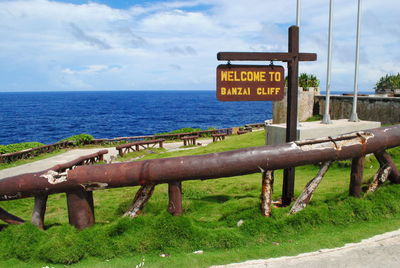 Information sign by sea against sky