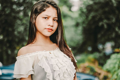 Close-up portrait of young woman standing against trees