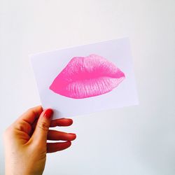 Close-up of hand holding paper with lipstick kiss against white background