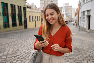 Brazilian young lady using mobile phone in city street of curitiba, parana, brazil