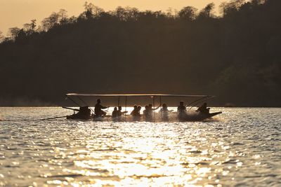 Silhouette people in boat on lake against sky