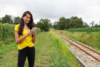 Young woman using mobile phone while standing on railroad track