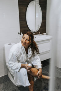 Woman holding camera while sitting against wall