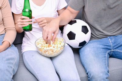 Midsection of friends with soccer ball having food and drink on sofa