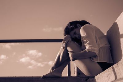 Young woman sitting on beach against sky