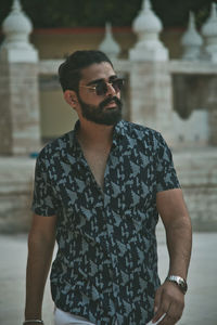 Young man wearing sunglasses standing against built structure