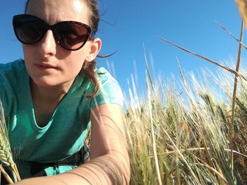 Portrait of young woman wearing sunglass on grassy field against sky