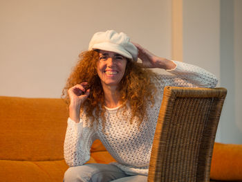 Portrait of smiling woman wearing hat sitting on chair at home