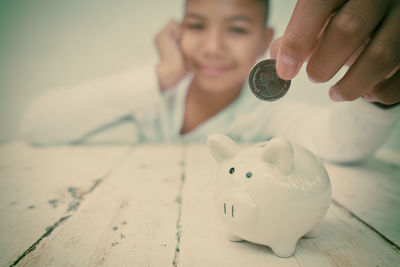Portrait smiling boy putting coin in piggy bank on table at home