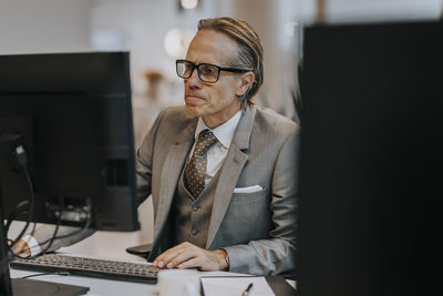 Mature businessman wearing eyeglasses using computer at desk in office