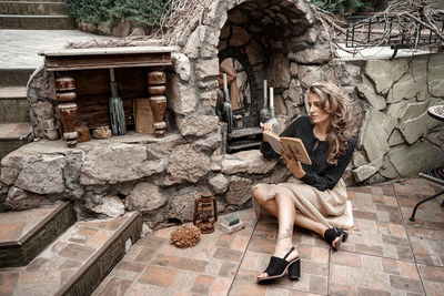 Full length of woman reading book while sitting outdoors